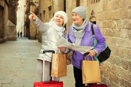 Happy mature ladies travellers with suitcases visiting sights of European city with mapの写真素材