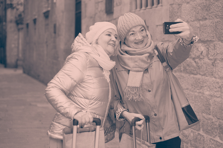 Happy elderly women tourists making selfie with phone during walk around cityの写真素材