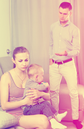 Portrait of quarreled husband and wife at home with litle boy on sofaの写真素材
