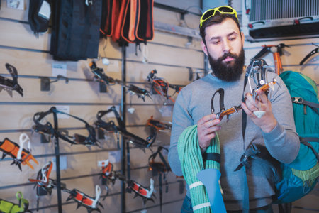 Young positive man choosing climbing equipment in sports equipment shop