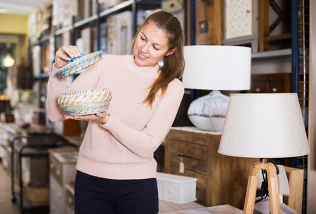 Positive woman buyer holding wicker basket in furniture storeの写真素材