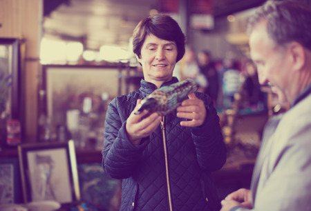 Mature woman is visiting the market of old things and choosing casket outdoorsの写真素材