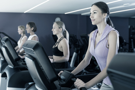 Four fit women running on treadmills in modern fitness clubの写真素材