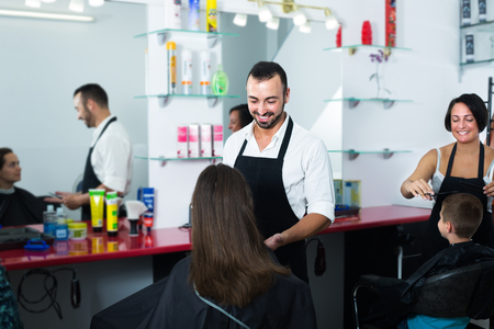 glad man hairdresser chatting to woman ready to cut her hair in crowded beauty salonの写真素材