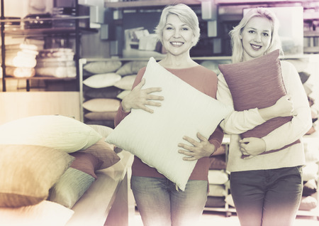 Happy cheerful  girl and mature woman customers showing bought pillows in home textile shopの写真素材