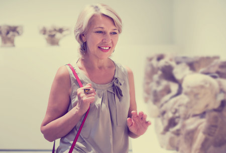 Portrait of mature woman visitor near sculpture in the historical museum