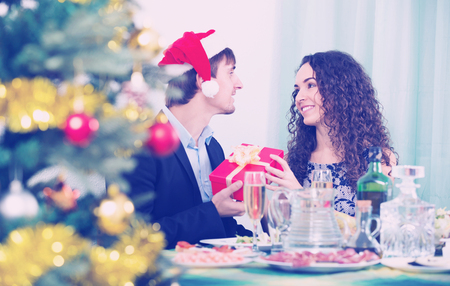Happy man giving present to smiling woman during Christmas dinner in homeの写真素材