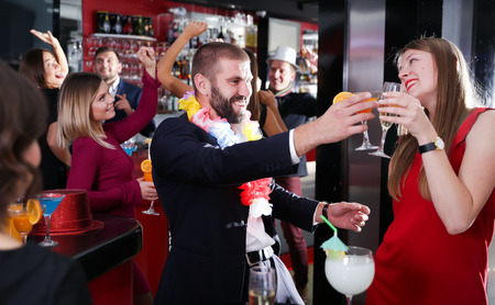 Young happy man with girlfriend having fun on Hawaiian party in barの写真素材