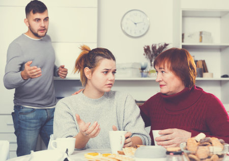 Senior woman asking upset girl to forgive her son after their quarrelの写真素材