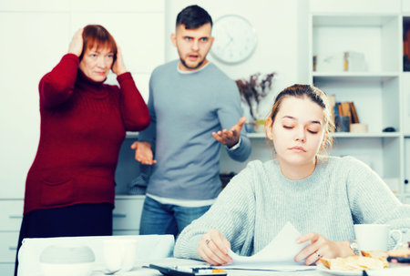 Upset girl sitting with documents while dissatisfied man with older woman standing behind her