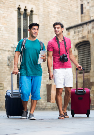 Two men are walking with luggage and watching to sights in Barcelonaの写真素材
