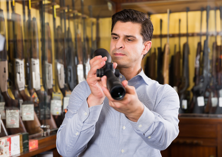 Young man looking for optical sights for hunting in shopの写真素材