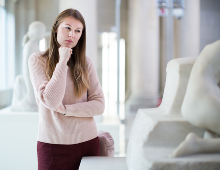 Girl looking with interest at ancient sculptures in art museum の写真素材
