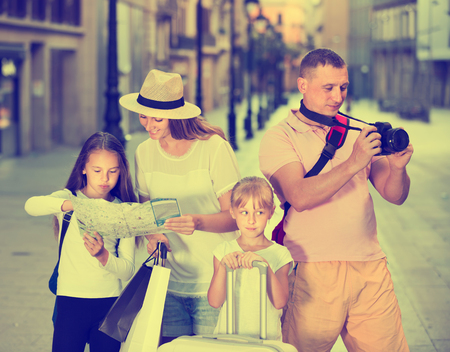 Smiling family with children using map and photographing sights during their vacationの写真素材