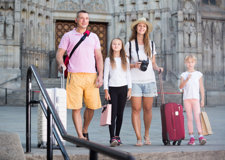Joyful family of tourists with two children walking around city with suitcasesの写真素材