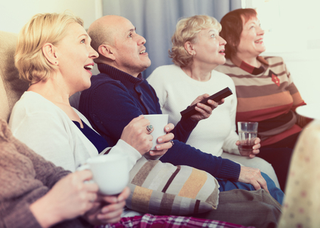 Mature friends are sitting on sofa and watching TV at home.の写真素材