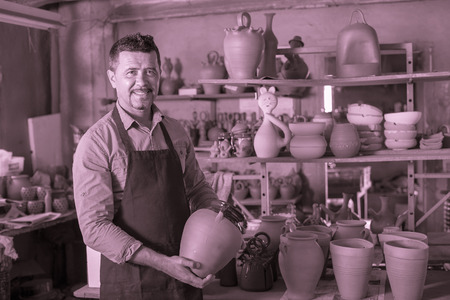 smiling mature male potter holding ceramics in hands  in workshopの写真素材