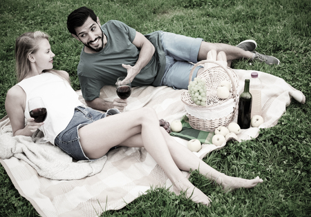 Smiling couple are talking and drinking wine in time picnic outdoorの写真素材