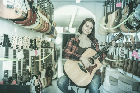 Young girl visitor is deciding on acoustic guitar in guitar shop.の写真素材