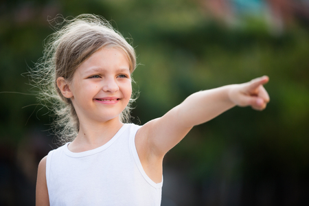 closeup portrait of happy girl in elementary school age pointing aside outdoors の写真素材