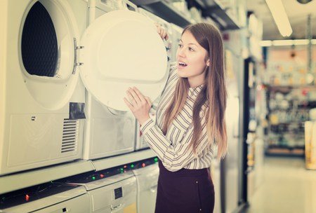 Positive girl looking for new clothes washer in store of kitchen appliancesの写真素材