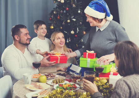 Happy family celebrating Christmas together at home, cheerful senior woman presenting gifts の写真素材