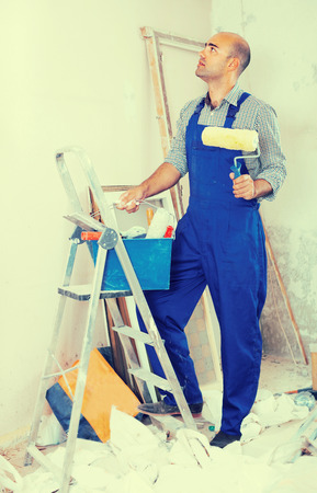 Professional constructor is standing with roller in uniform near the stepladder. の写真素材