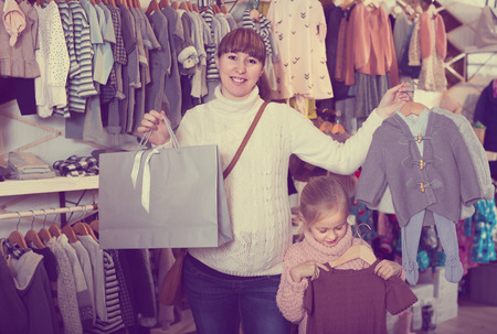 Pretty pregnant mother and girl enjoying their purchases in childrenâs cloths shopの写真素材