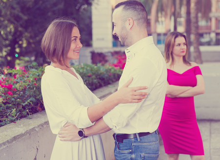 Young woman is flirting with boyfriend when her girlfriend is envying them outdoors.の写真素材