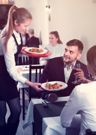 Woman waiter is giving dish to client in restaurante indoor.の写真素材