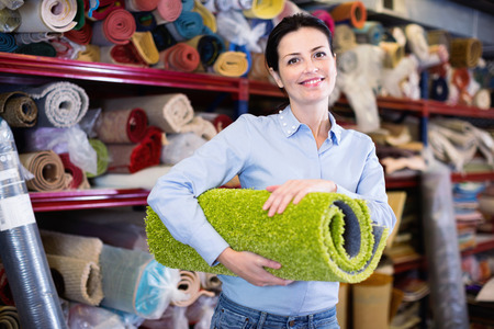Cheerful smiling woman consumer shopping and holding carpet indoorsの写真素材