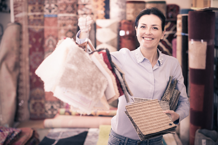 Happy woman shopping carpet and showing samples in interior storeの写真素材