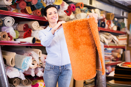 happy young buyer standing and choosing in shop with colour carpetsの写真素材