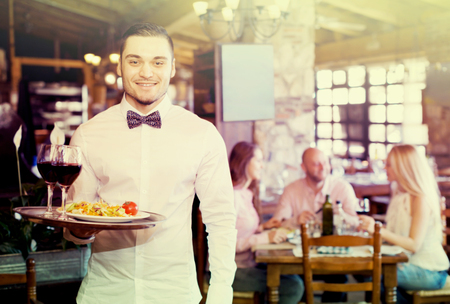 Portrait of a happy male waiter with a tray in his hand at the restaurantの写真素材
