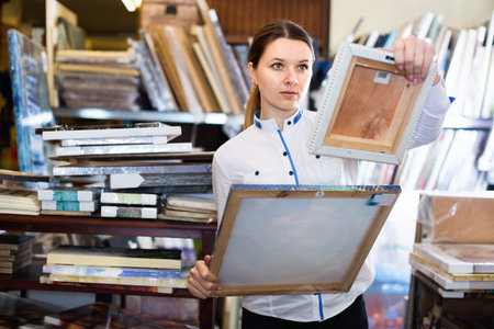 Happy cheerful positive woman is choosing new picture for her home in the store.