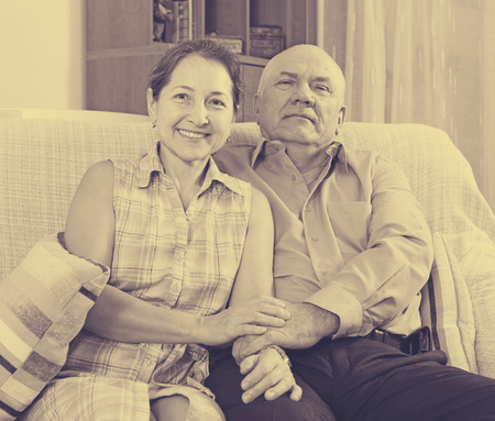 Happy mature couple sitting on couch together in homeの写真素材