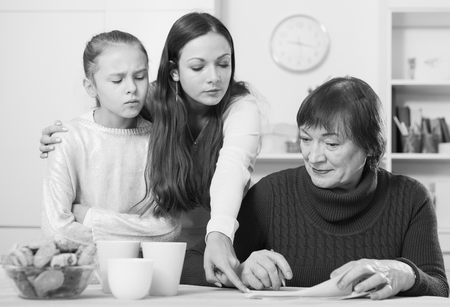Young serious woman with her daughter pointing to some paper to elderly motherの写真素材
