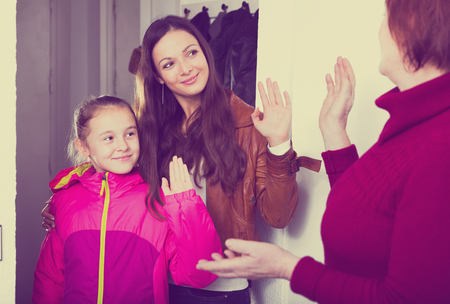Happy young mother with little daughter leaving apartment saying goodbye to grandmotherの写真素材