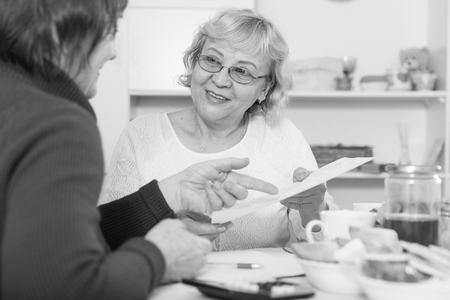Two positive mature women considering papers while sitting on kitchenの写真素材