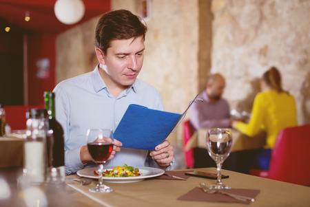 Adult man choosing dishes out of menu card in restaurantの写真素材