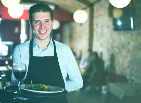 Handsome adult waiter with serving tray welcoming to restaurantの写真素材