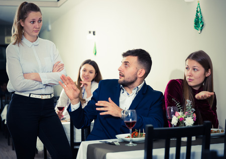 Young woman is dissatisfied in time her boyfriend is talking with woman in restaurante indoor.の写真素材
