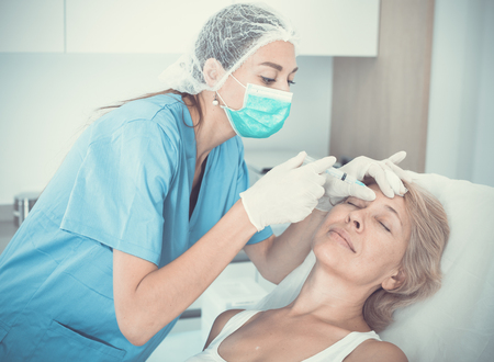 Mature female client receiving cosmetic injection from professional cosmeticianの写真素材