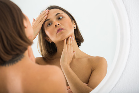Young woman looking in mirror in bedroom in morningの写真素材