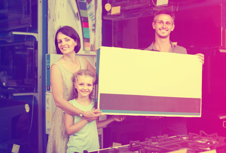 happy couple with girl shopping new electronics and holding box in shop of household appliancesの写真素材
