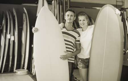 Young man with girl demonstraiting surfboard in shop in time summer holidaysの写真素材