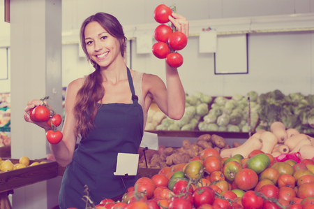 smiling young woman seller showing fresh ripe tomatoes in food store
の写真素材