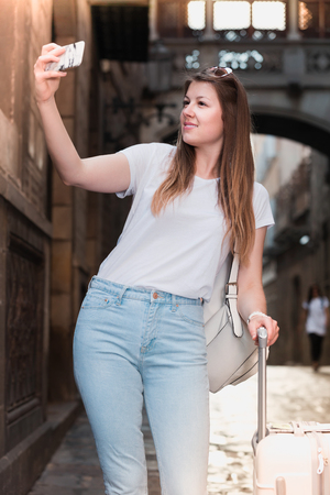 Positive young female with luggage doing selfie on vacationの写真素材