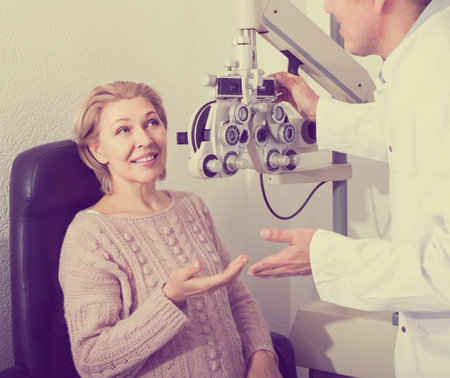 smiling european  mature optician examinating eyesight with aid of slit lamp の写真素材