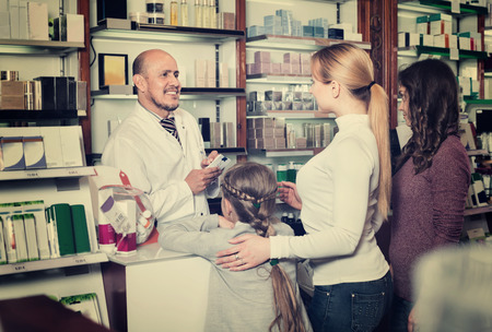 Smiling  diligent male pharmacist in white coat working the pharmaceutical store and consulting customersの写真素材
